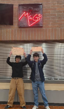 Protestors Thomas Tran and Alejandro Ceja stand under the school store sign, holding their signs reading “Keep Popcorners One Dollar” and “Hands off Our Popcorners. Keep Popcorners 1$” respectively.