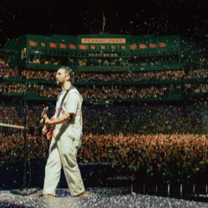The album cover for Live From Fenway Park depicts Noah Kahan playing the guitar and singing his heart out as around 38,000 people shout the lyrics back to him at Fenway Park in July of 2024.